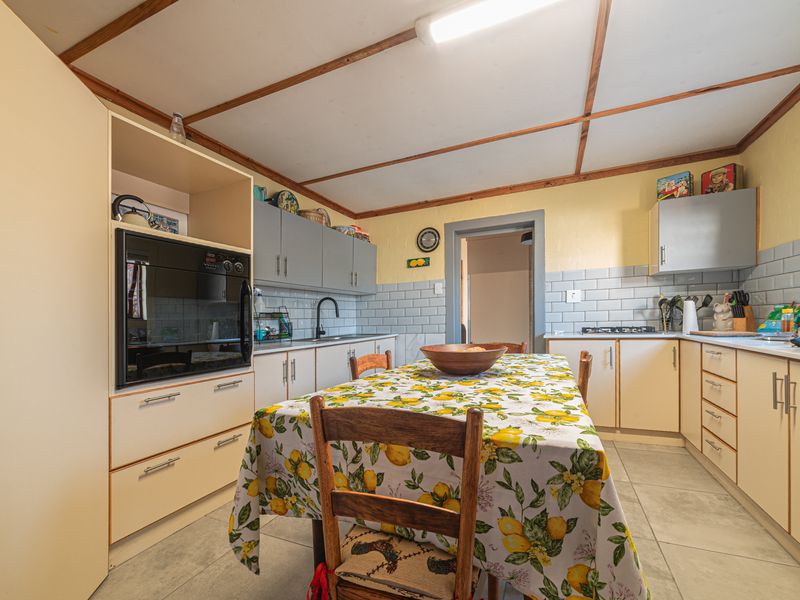 A functional kitchen featuring built-in cabinetry, subway tile backsplash, integrated oven, gas hob, and tiled flooring with exposed timber ceiling beams.