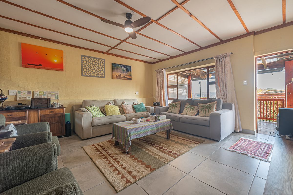 A comfortable living room featuring exposed timber ceiling beams, a ceiling fan, and tiled flooring, with direct access to an outdoor patio area.