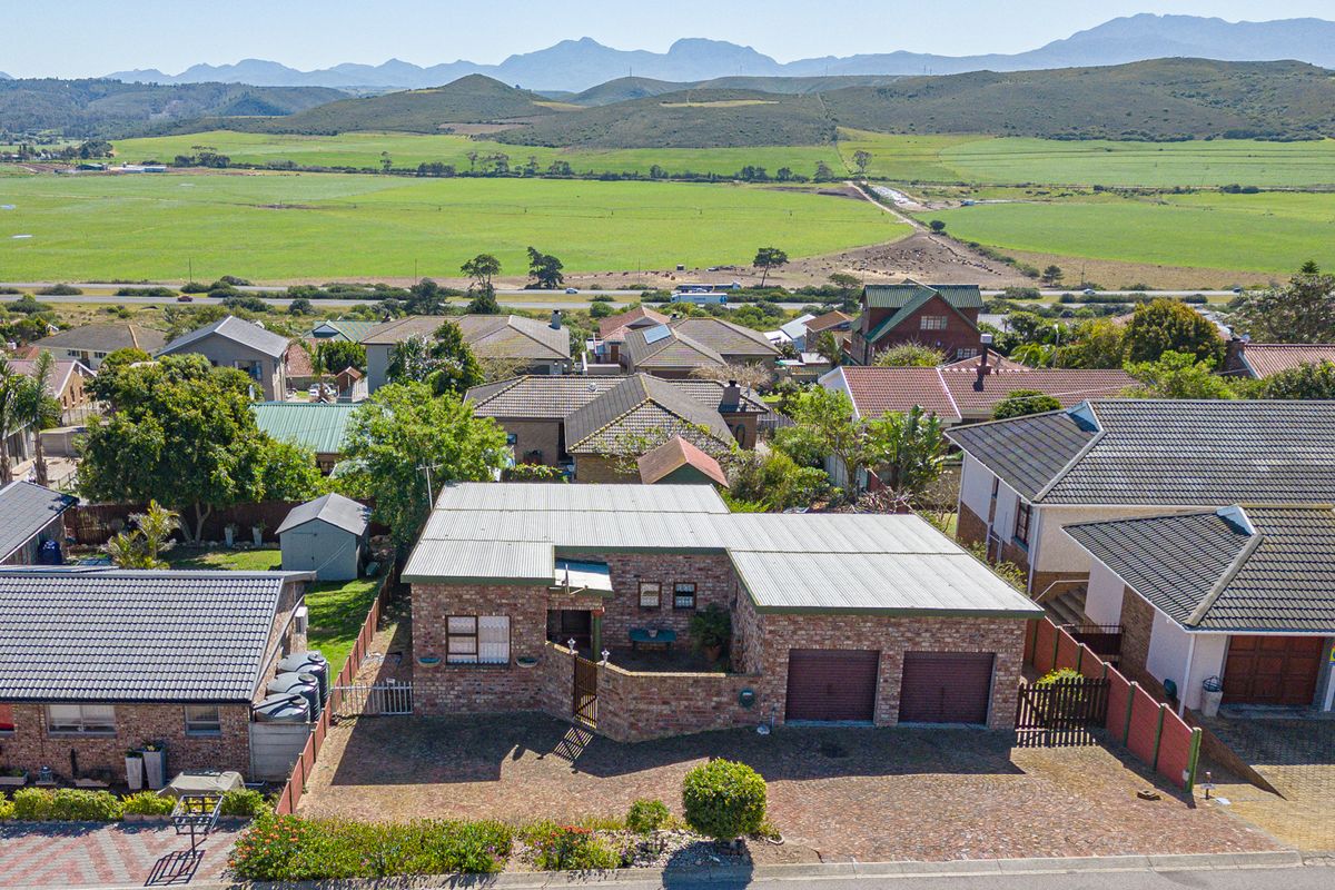 Aerial view of a residential property featuring a brick exterior, double garage, and paved driveway, set against a scenic rural landscape.