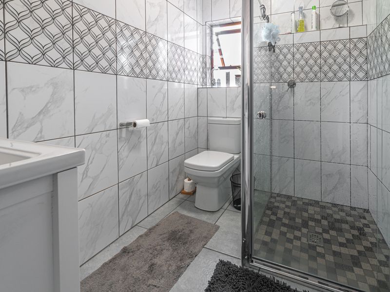 A modern bathroom featuring a glass-enclosed shower, toilet, and vanity basin with contemporary marble-effect wall tiling and patterned accent tiles.