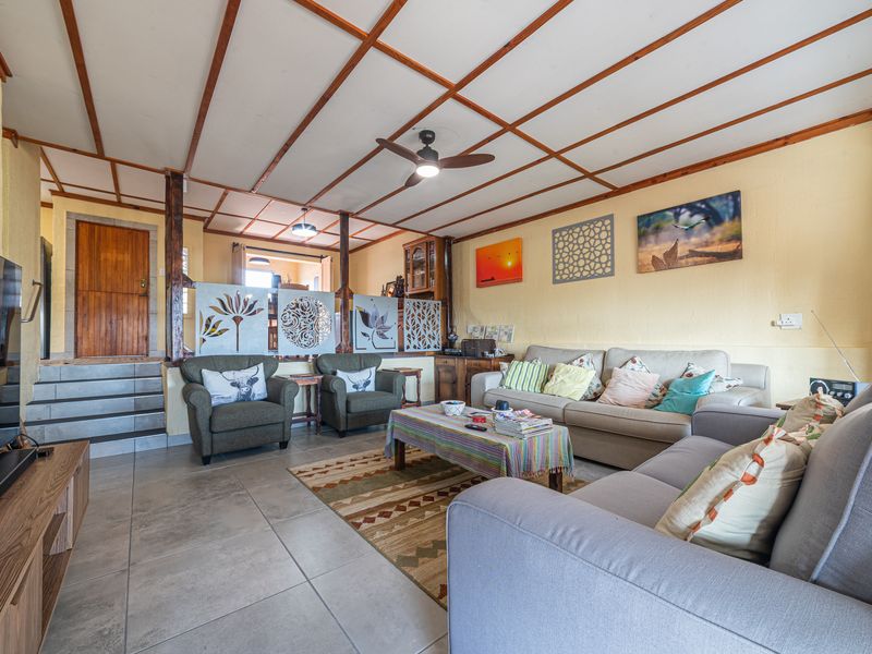 Spacious living room featuring tiled flooring, exposed timber ceiling beams, and a decorative room divider leading to an elevated internal area.