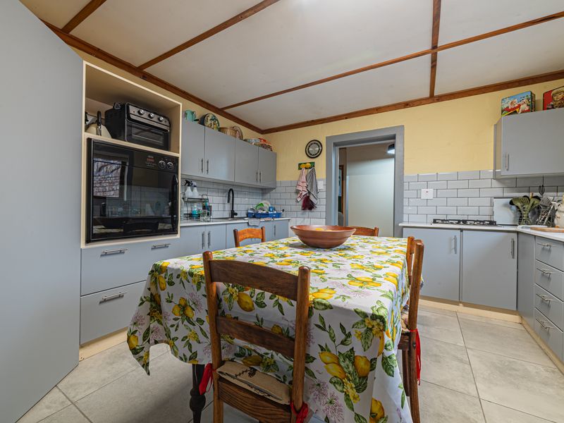 Functional kitchen featuring grey cabinetry, subway tile backsplash, built-in oven, gas hob, and tiled flooring with an exposed beam ceiling.