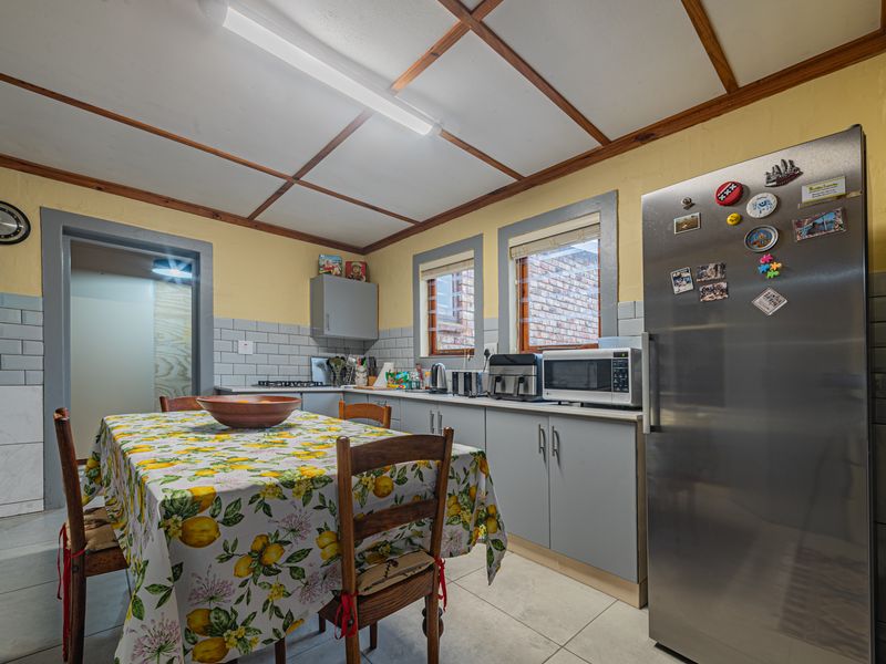 A functional kitchen featuring grey cabinetry, subway tile backsplash, tiled flooring, and exposed timber ceiling beams, offering a practical layout for daily use.