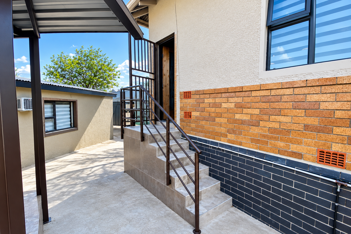 A well-maintained rear exterior area featuring a tiled staircase with metal handrails, brick facade detailing, and secure aluminium window frames.