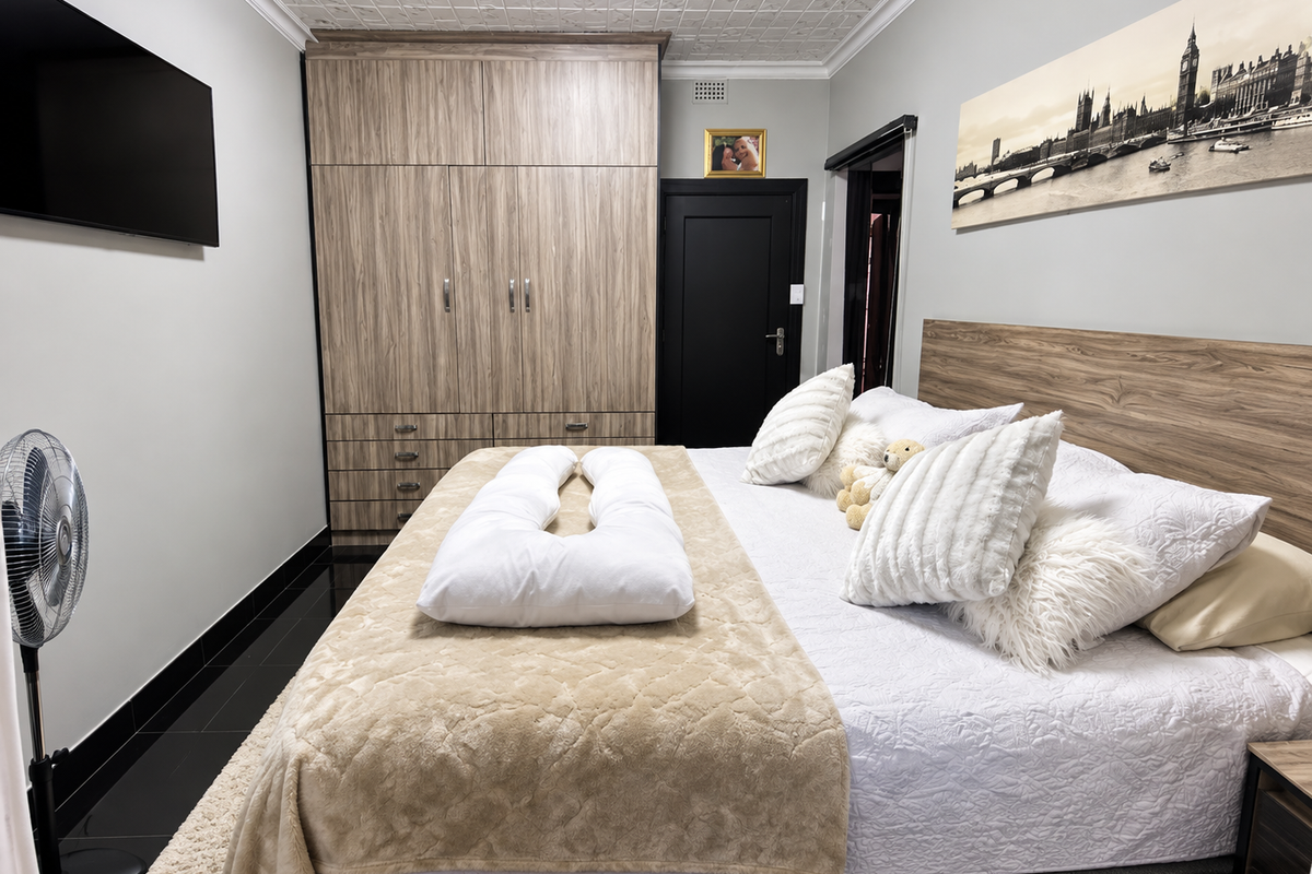 A well-maintained bedroom featuring built-in wood-grain wardrobes, decorative ceiling tiles, and dark tiled flooring, providing a clean and functional living space.