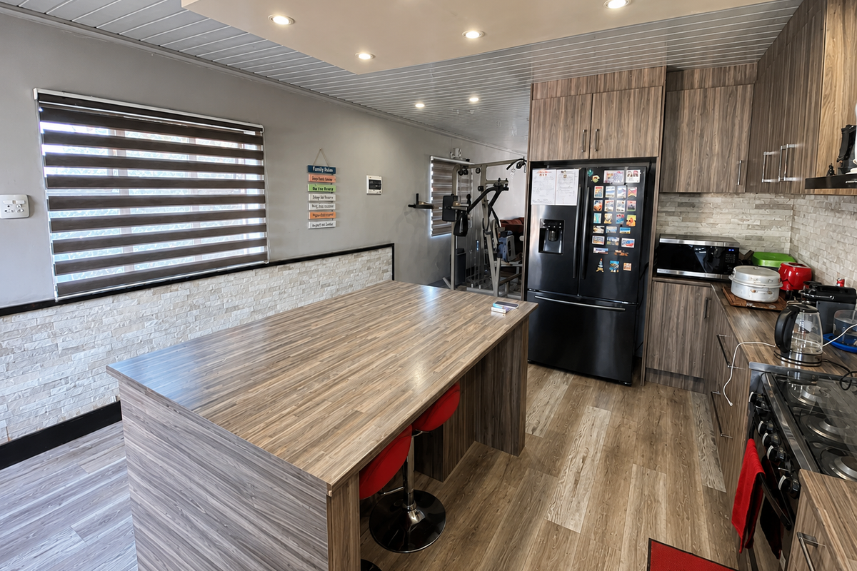 Modern kitchen featuring wood-grain cabinetry, a central island, stone veneer accents, recessed lighting, and integrated appliances, with an adjacent open-plan living area.