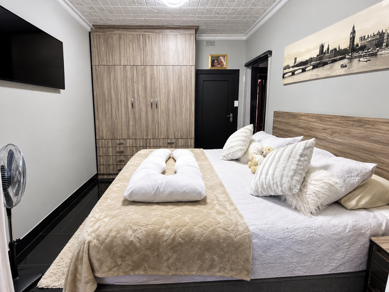 A well-maintained bedroom featuring built-in wood-grain wardrobes, decorative ceiling tiles, and dark tiled flooring, providing a clean and functional living space.