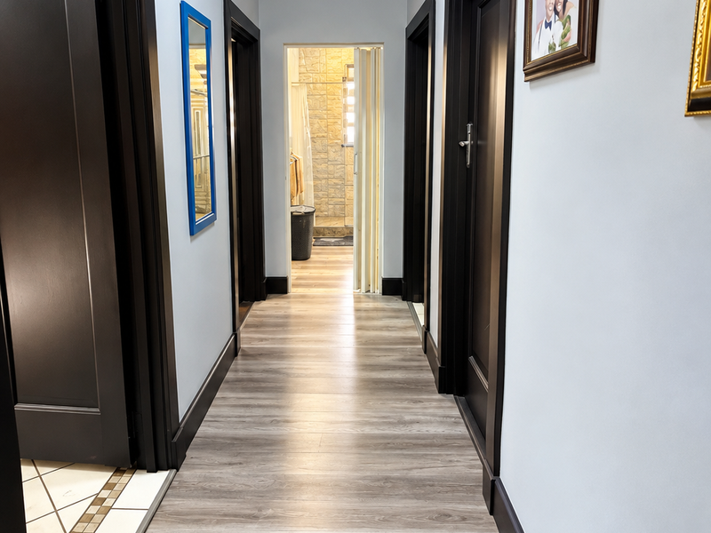 A well-maintained hallway featuring modern laminate flooring, dark wood-toned door frames, and a clean tongue and groove ceiling design.