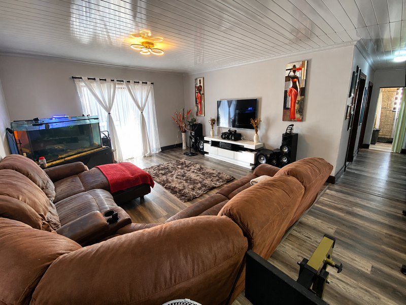 Spacious living room featuring wood-look laminate flooring, a tongue and groove ceiling, and a sliding glass door providing natural light.