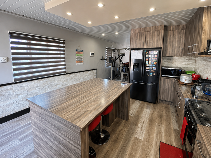 Modern kitchen featuring wood-grain cabinetry, a central island, stone veneer accents, recessed lighting, and integrated appliances, with an adjacent open-plan living area.