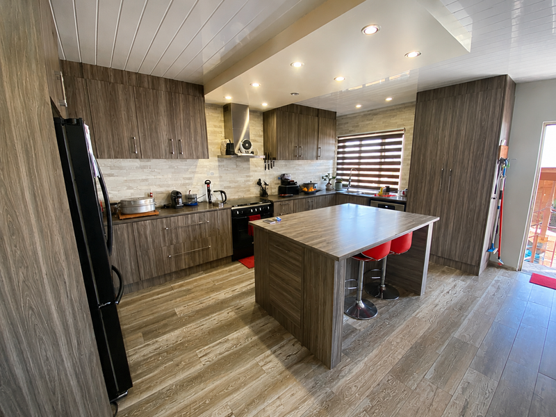 Modern kitchen featuring wood-grain cabinetry, a central island, stone-look backsplash, and integrated stainless steel appliances with recessed lighting.