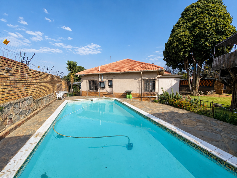 Outdoor pool area featuring a swimming pool with stone paving, enclosed by a brick boundary wall and security fencing.