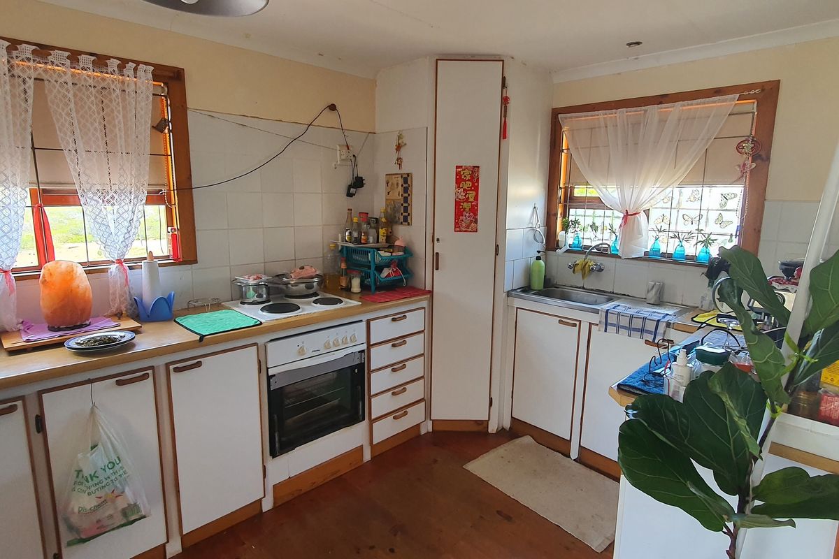 A dated kitchen featuring white cabinetry, timber flooring, an electric stove, and a stainless steel sink with tiled splashbacks.