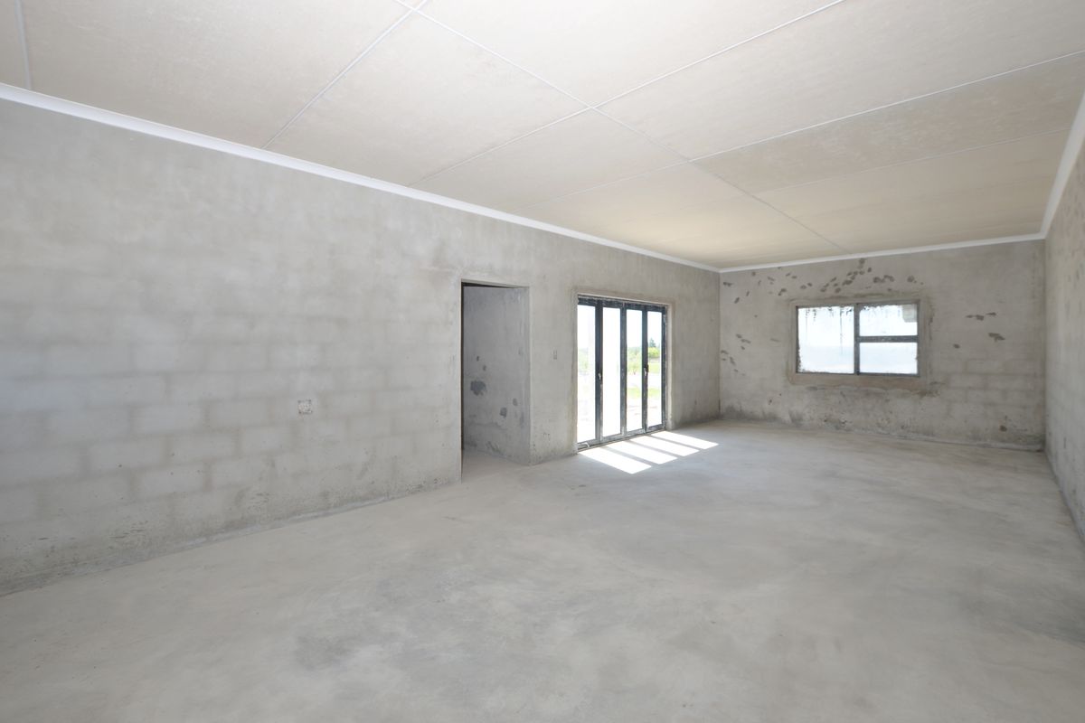 An expansive, unfinished interior space featuring raw concrete walls, a tiled ceiling, and large glass sliding doors leading to the exterior.
