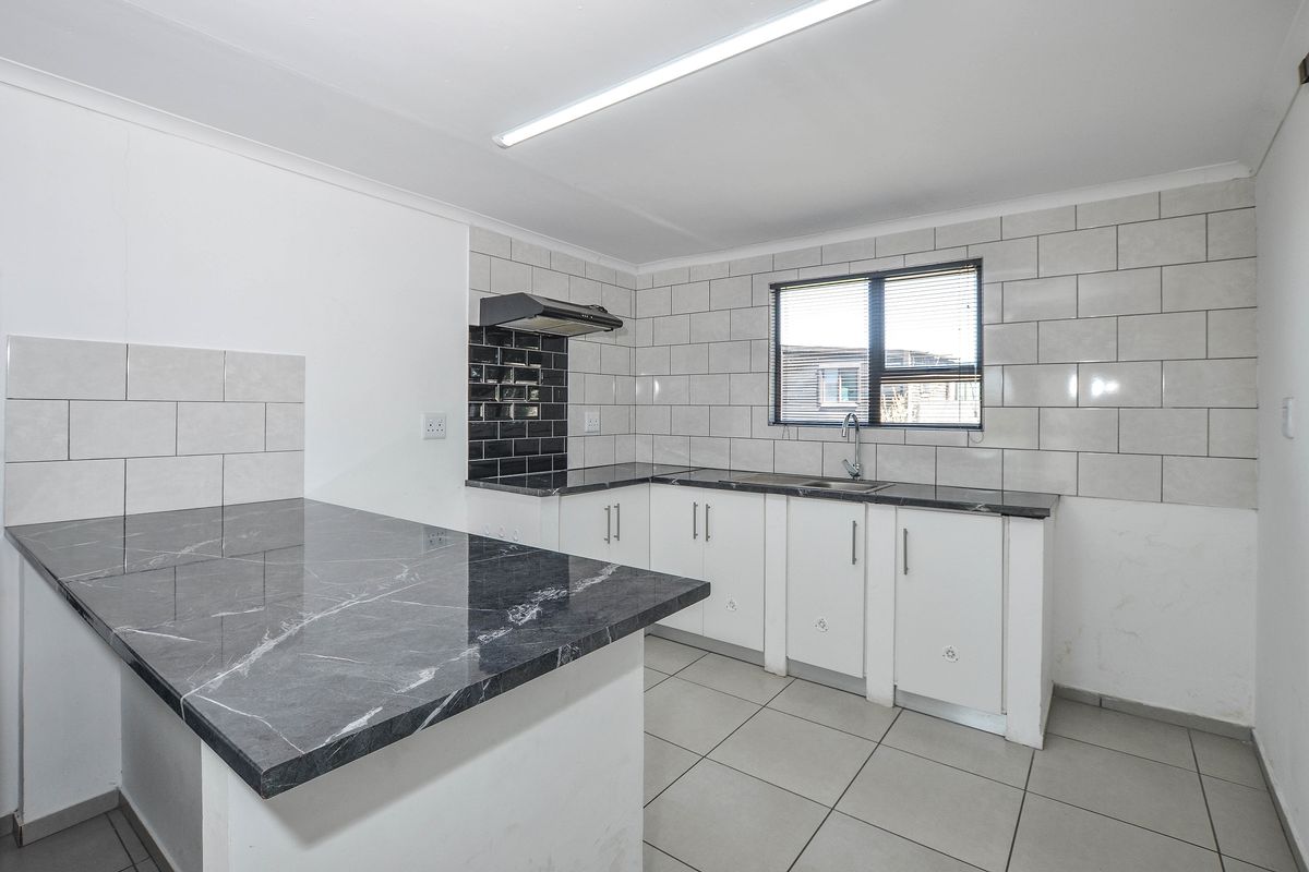 A functional kitchen featuring white cabinetry, dark marble-effect countertops, subway tile backsplash, and tiled flooring with an integrated breakfast bar area.