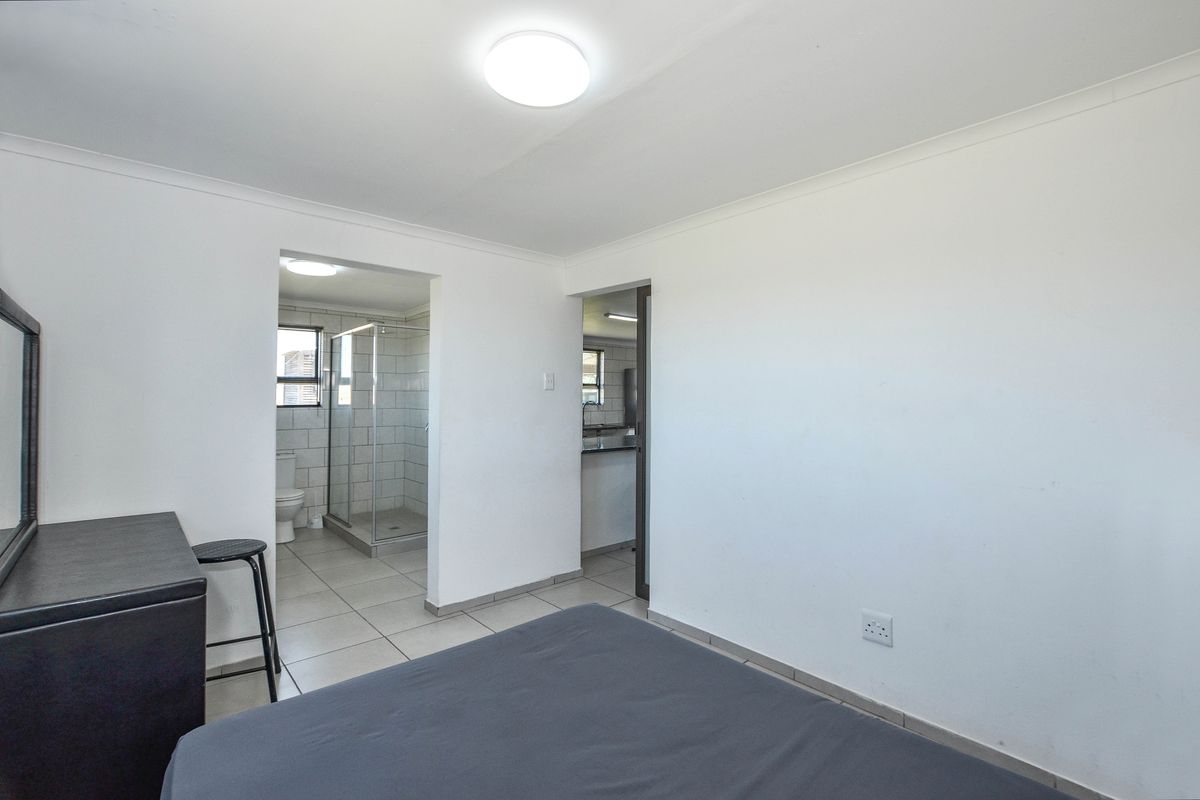 A bedroom featuring tiled flooring and an en-suite bathroom with a glass-enclosed shower, providing a functional and clean living space.