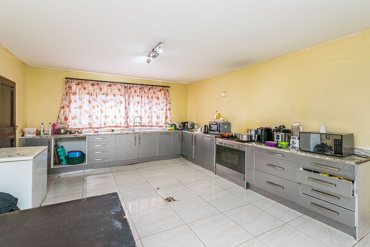 A spacious kitchen featuring grey cabinetry, stone countertops, a built-in oven, and tiled flooring, offering a functional layout in need of cosmetic updates.