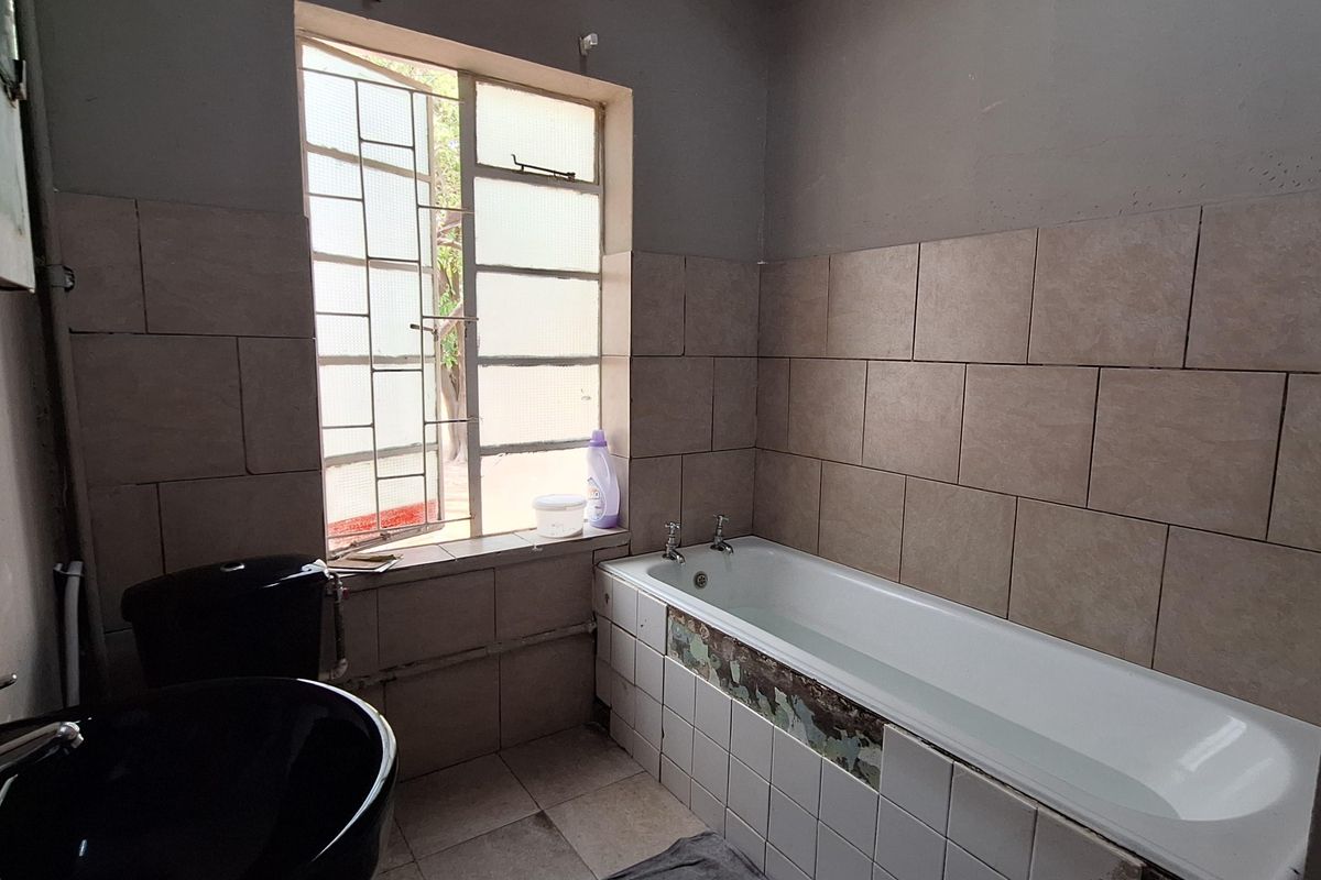 A dated bathroom featuring a standard bathtub with tiled surround, a black basin, and a window with security bars.