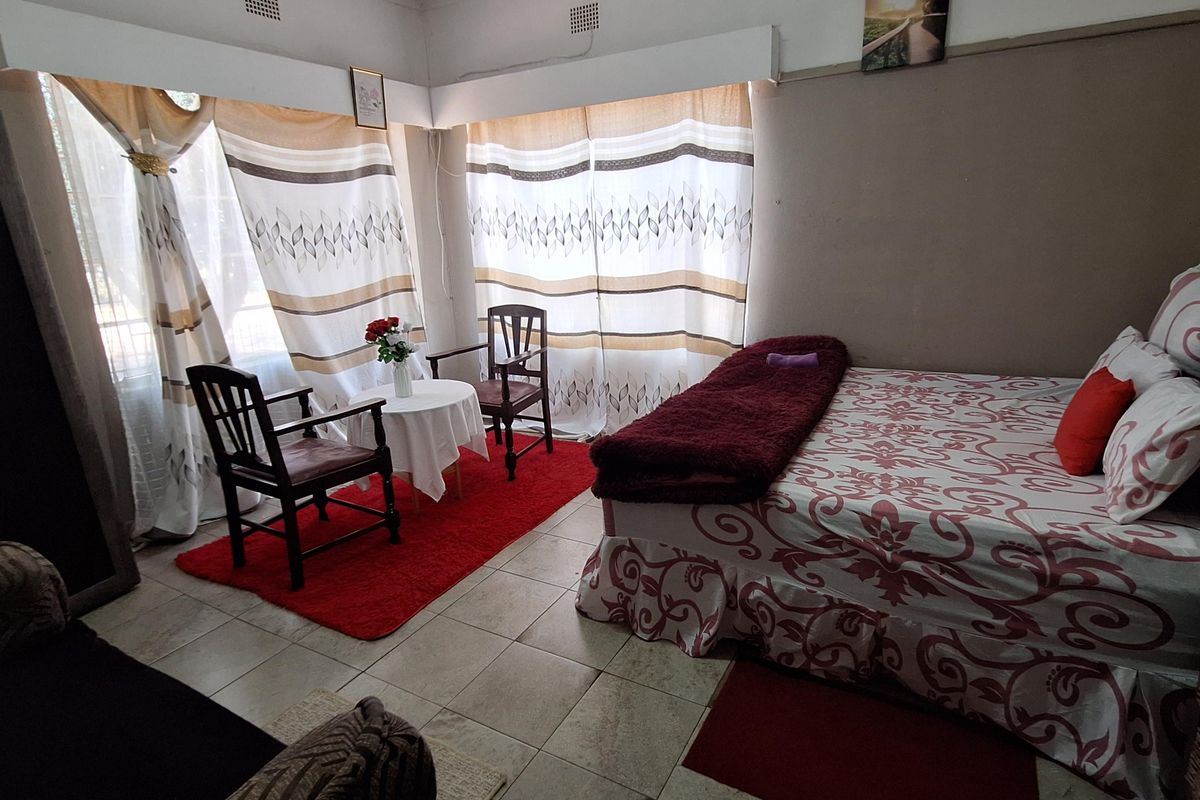 A bedroom featuring tiled flooring and large windows with curtains, providing natural light. The space includes built-in ceiling ventilation grilles.