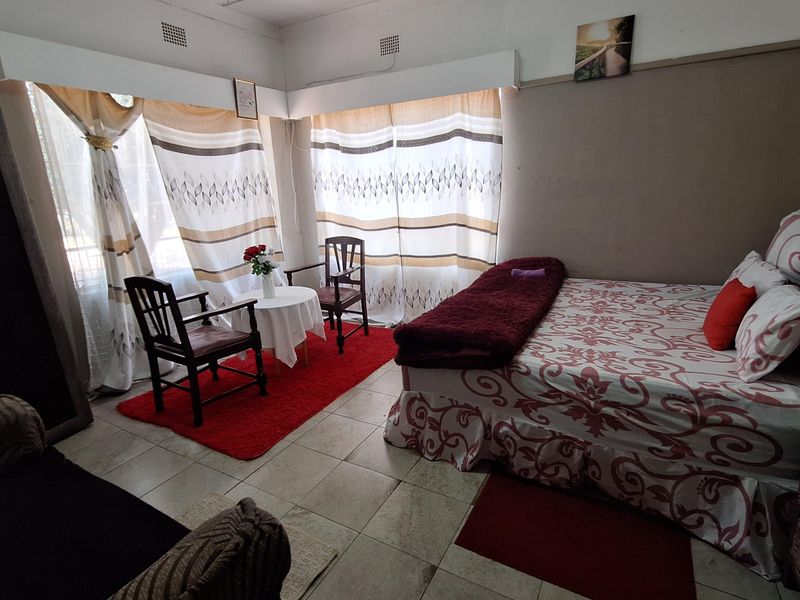 A bedroom featuring tiled flooring and large windows with curtains, providing natural light. The space includes built-in ceiling ventilation grilles.
