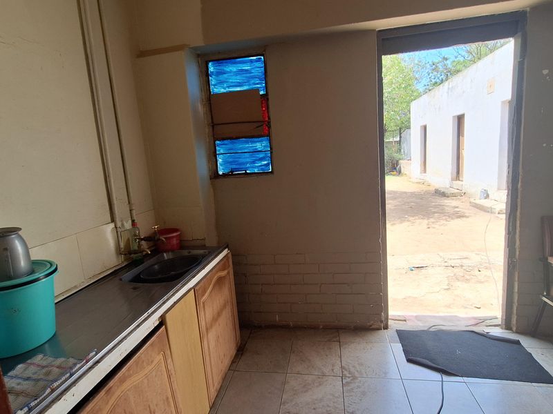 A functional scullery or utility area featuring a built-in sink unit, tiled flooring, and direct access to the rear exterior of the property.