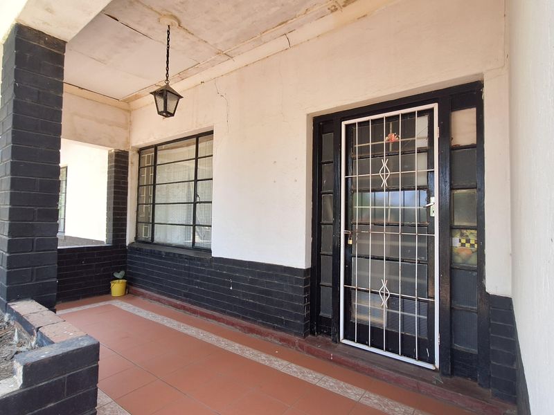 Covered front porch featuring tiled flooring, brick pillar accents, and a security gate entrance.