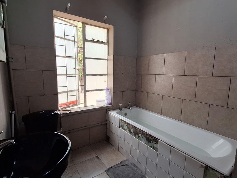 A dated bathroom featuring a standard bathtub with tiled surround, a black basin, and a window with security bars.