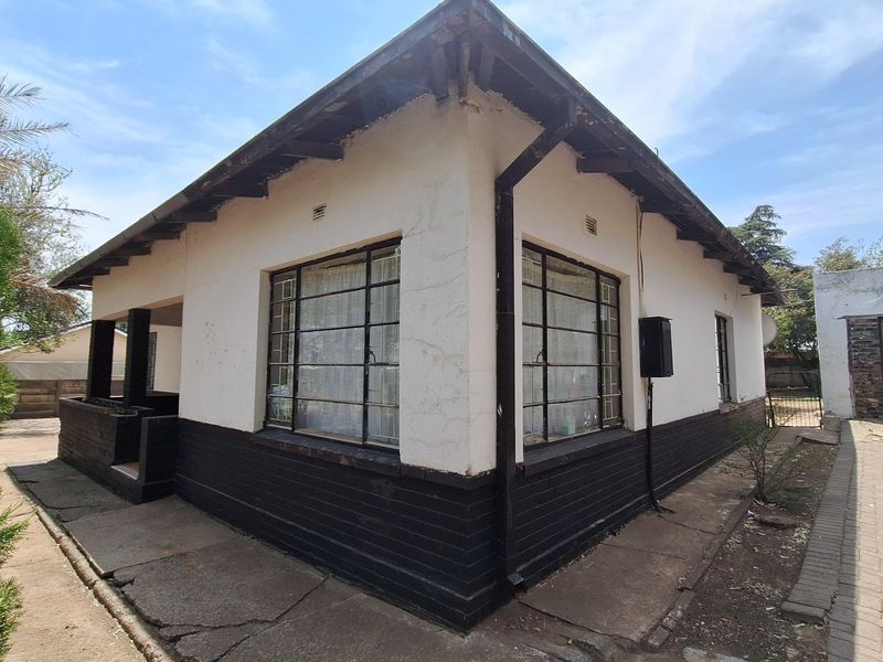 Exterior view of a single-story house featuring a two-tone painted facade, steel-framed windows, and surrounding concrete paving in need of maintenance.