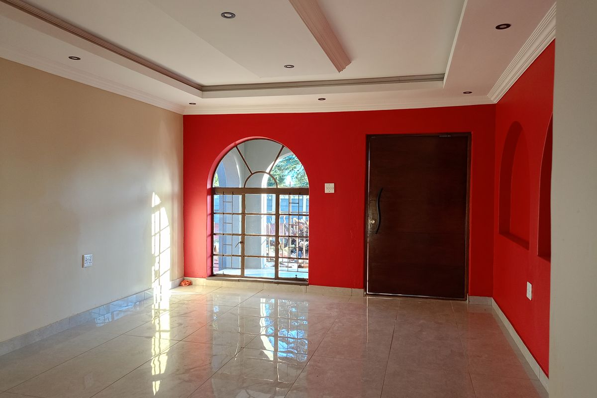 A bright, empty living room featuring tiled flooring, a decorative arched window, recessed ceiling lighting, and a solid timber entrance door.