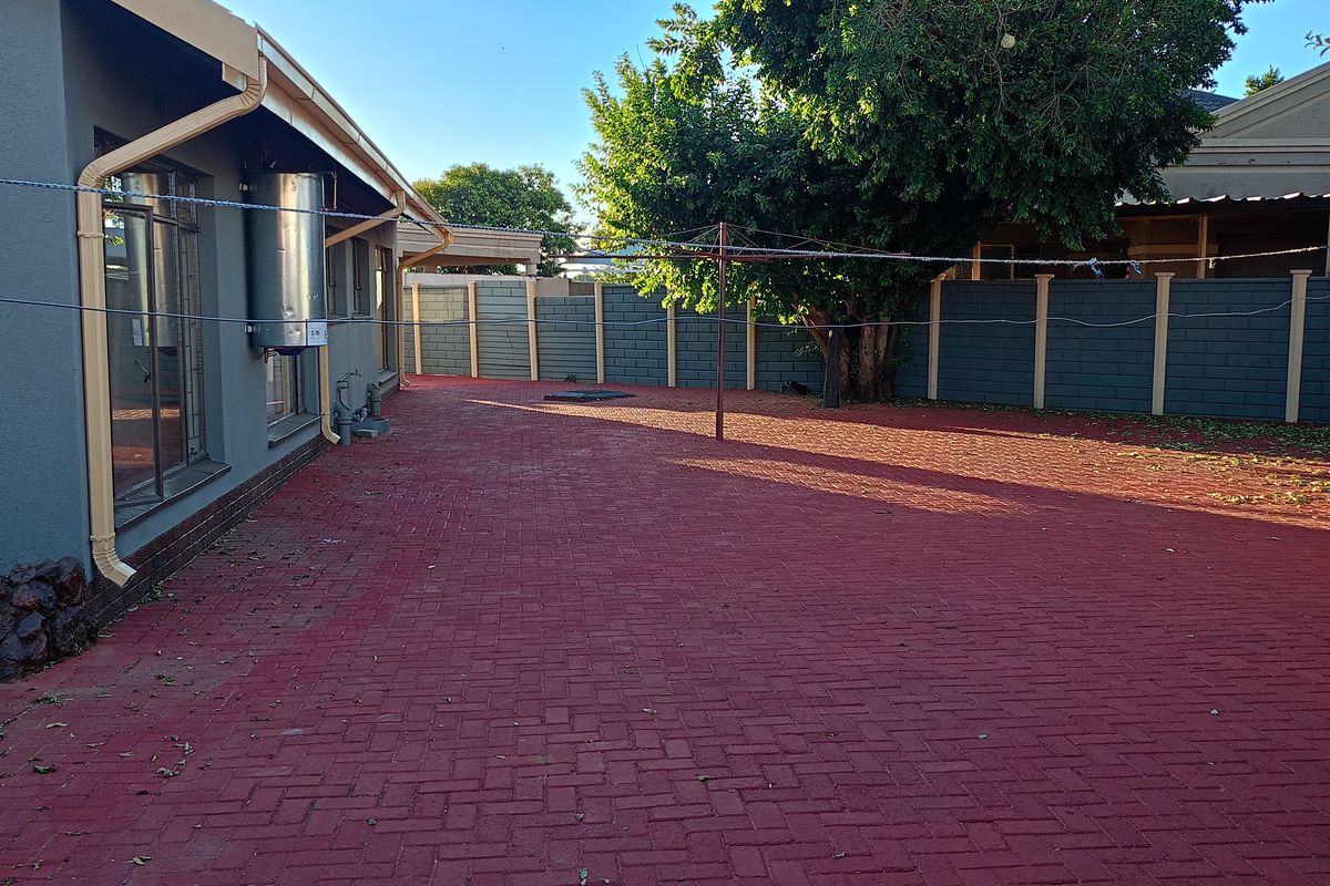 Spacious rear courtyard featuring red brick paving, perimeter boundary walls, and a large mature tree providing shade.