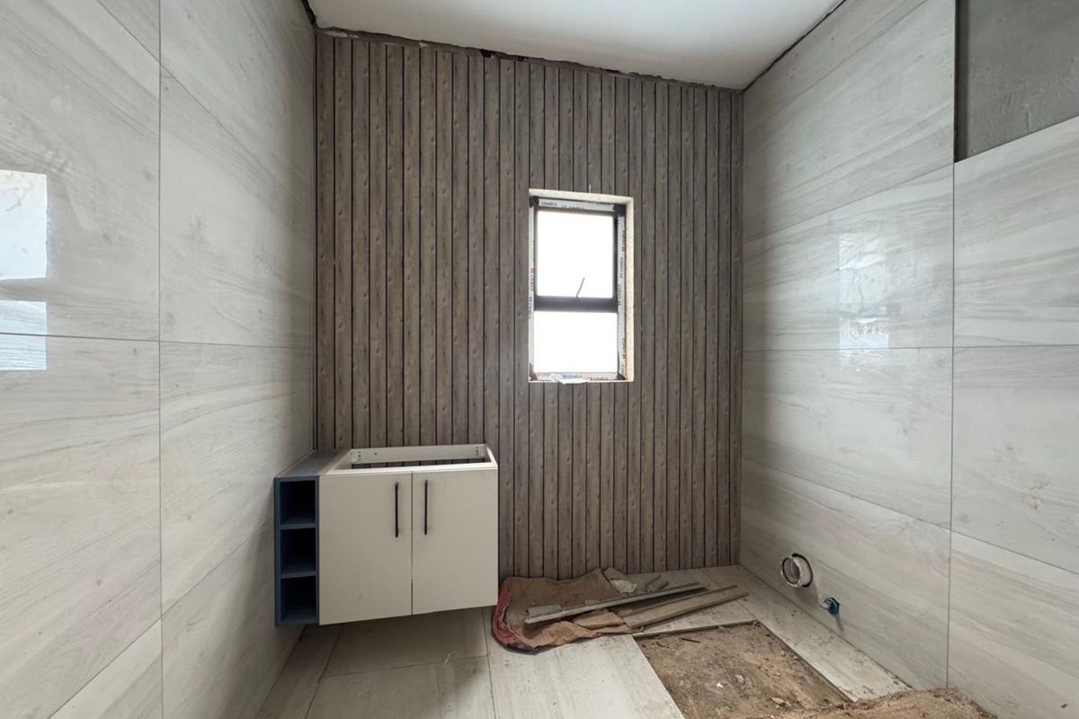 A bathroom under renovation featuring wood-look wall paneling, light-toned wall tiles, and a partially installed vanity cabinet with exposed plumbing.