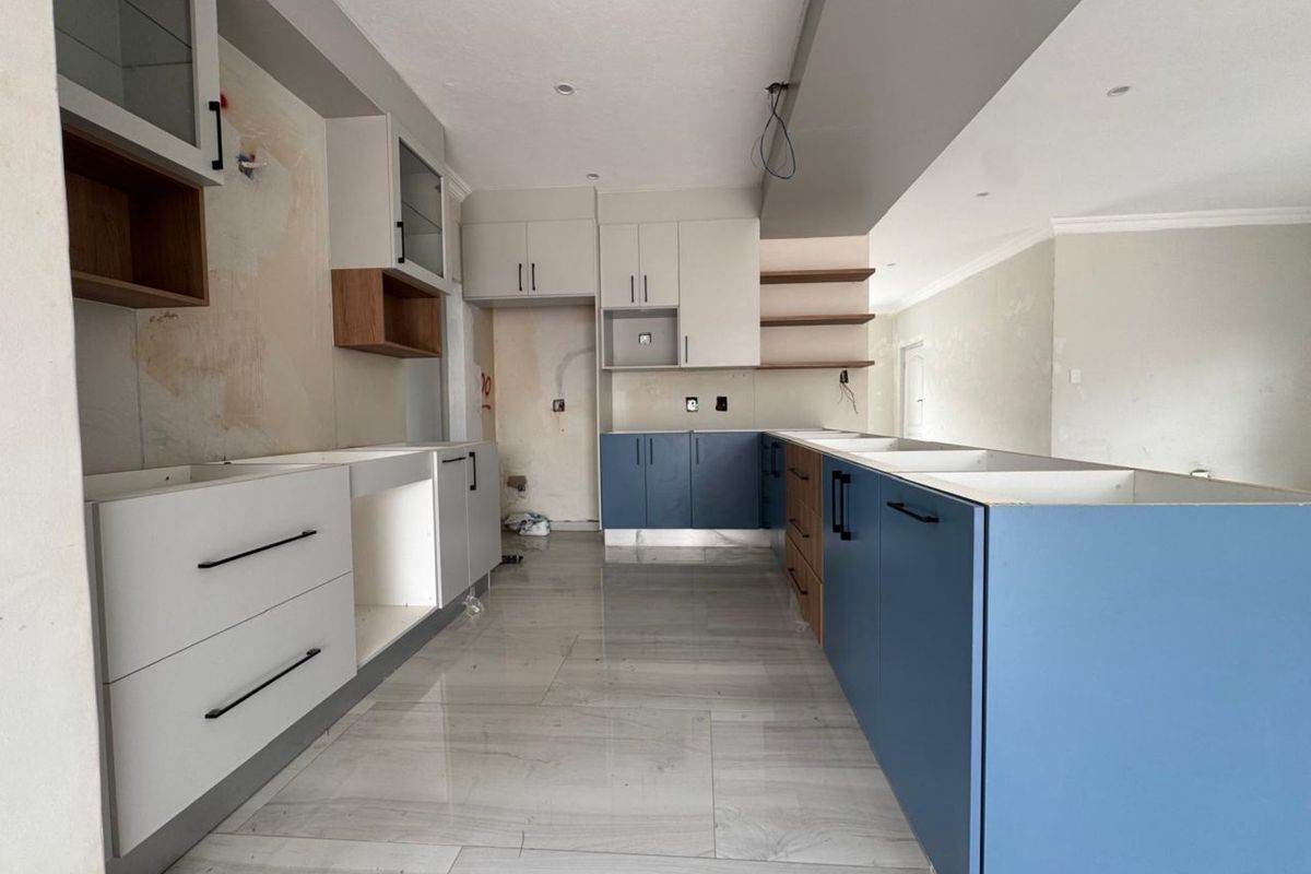 An unfinished kitchen space featuring modern two-tone cabinetry, large format floor tiles, and open shelving, currently awaiting final installation and wall finishing.