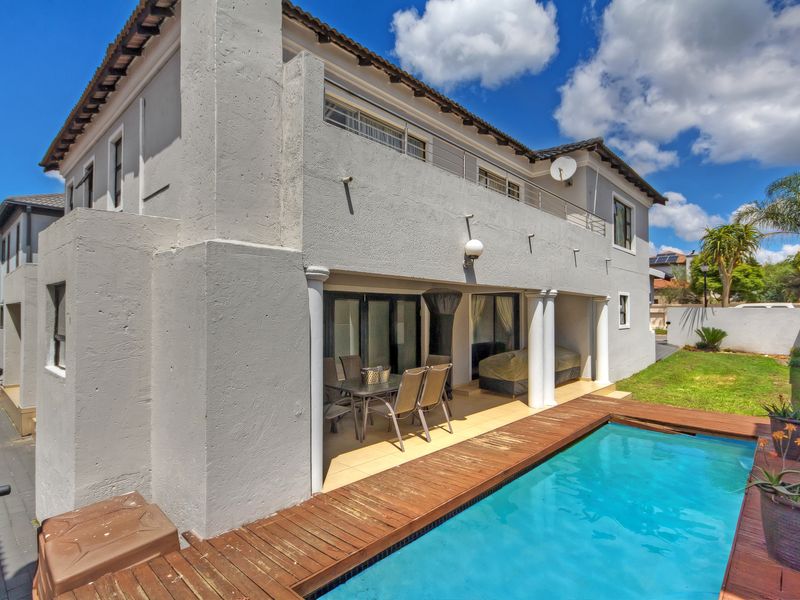 Rear view of the property featuring a swimming pool with a wooden deck, a covered patio area, and an upper-level balcony.