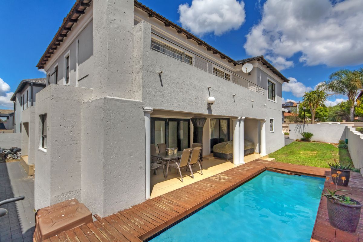 Rear view of the property featuring a swimming pool with a wooden deck, a covered patio area, and an upper-level balcony.