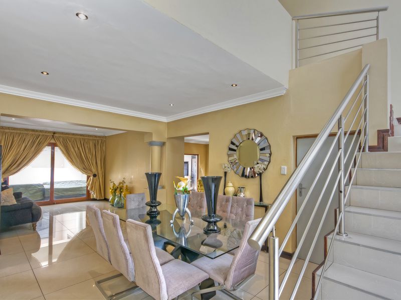 Spacious open-plan dining area featuring tiled flooring, recessed lighting, and a modern staircase with stainless steel railings leading to the upper level.