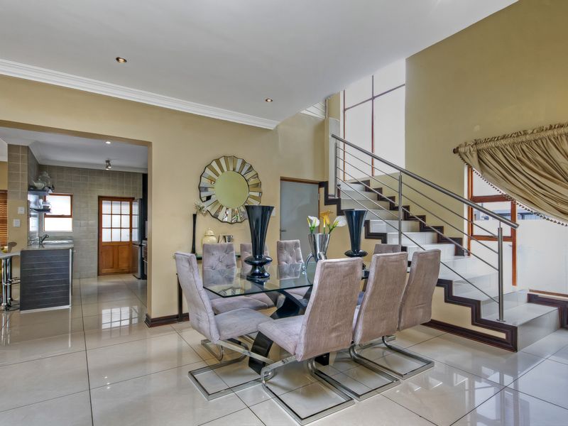 Spacious open-plan dining area featuring polished tile floors, a modern staircase with stainless steel railings, and seamless flow into the adjacent kitchen.