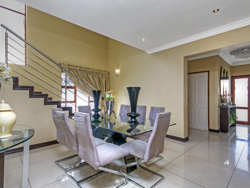 A well-maintained dining area featuring tiled flooring, crown molding, and a modern staircase with a stainless steel balustrade.