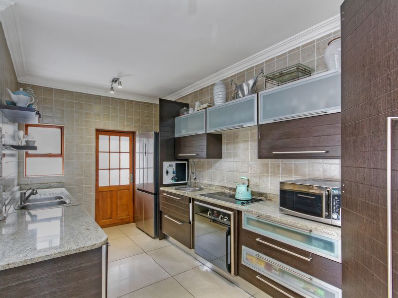 A functional kitchen featuring dark wood cabinetry, granite countertops, a tiled backsplash, and integrated appliances, offering a clean and well-maintained workspace.