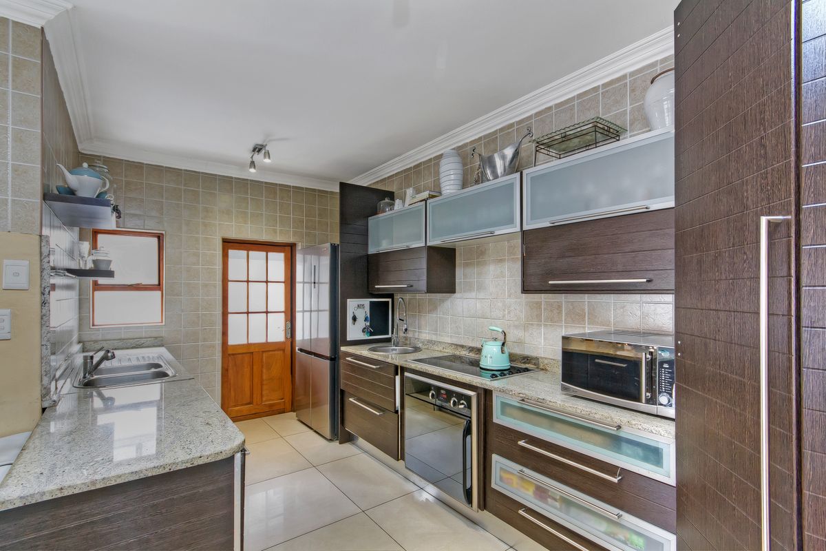 A functional kitchen featuring dark wood cabinetry, granite countertops, a tiled backsplash, and integrated appliances, offering a clean and well-maintained workspace.