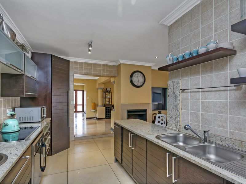 Functional kitchen featuring granite countertops, double stainless steel sink, built-in oven, electric hob, and ample cabinetry with a tiled backsplash.