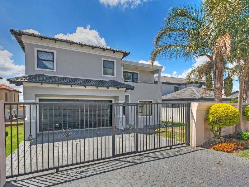 A well-maintained double-story residential property featuring a paved driveway, secure wrought iron gate, double garage, and a balcony.