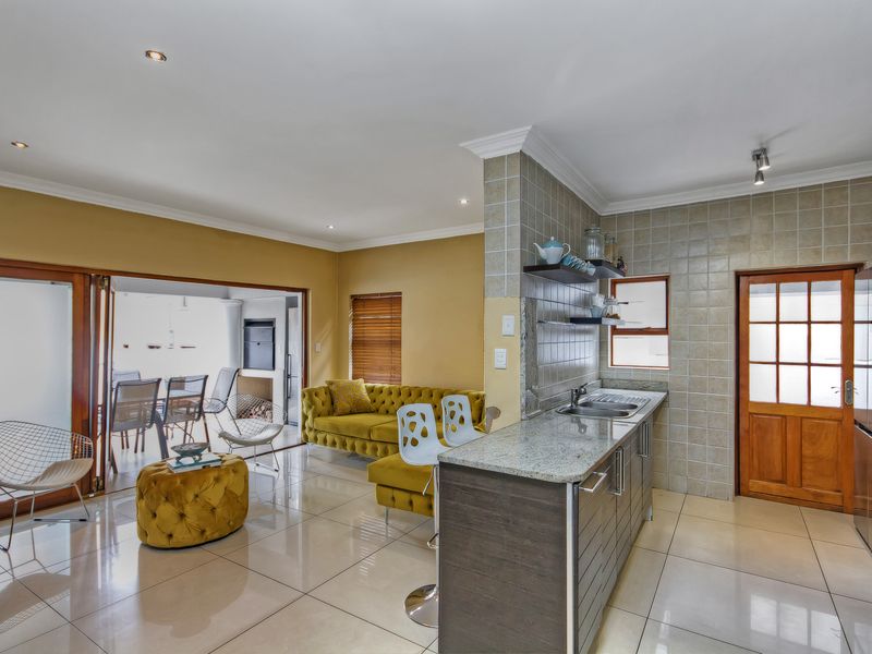 Open-plan living area featuring a modern kitchen with granite countertops, tiled flooring, and seamless flow to an outdoor patio through folding glass doors.