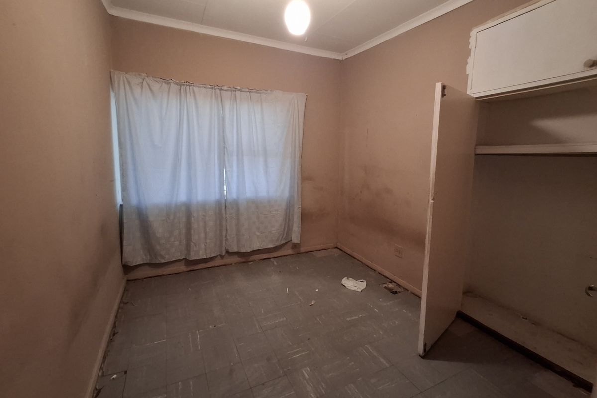 A vacant bedroom featuring built-in storage, tiled flooring, and a window, requiring cosmetic updates and refurbishment to restore its condition.