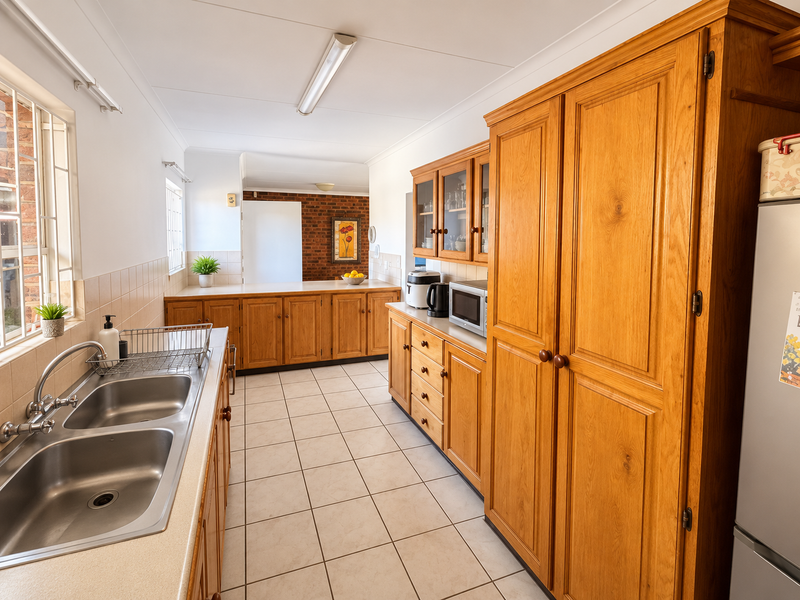 A functional kitchen featuring extensive wooden cabinetry, double stainless steel sink, tiled flooring, and a neutral backsplash, offering a classic and practical layout.