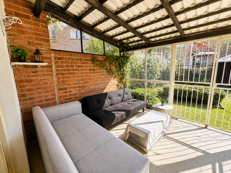 A covered patio area featuring exposed brick walls, a timber-framed roof, and secure metal gating overlooking the garden.
