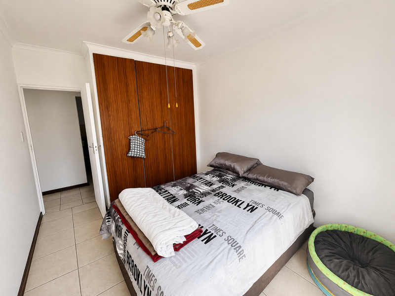 A bedroom featuring tiled flooring, a built-in wooden wardrobe, and a ceiling fan.