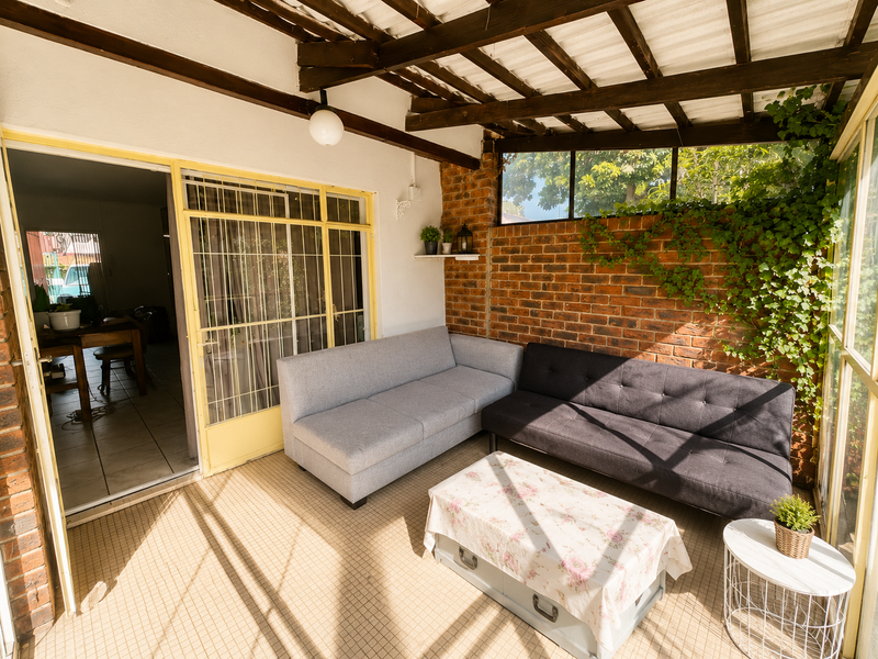 A covered patio area featuring exposed timber rafters, a rustic brick feature wall, and tiled flooring, providing a comfortable outdoor living space.