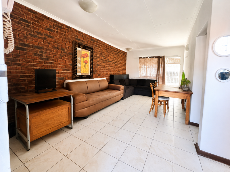 A living area featuring an exposed brick feature wall, neutral ceramic floor tiles, and direct access to an outdoor space via a sliding glass door.