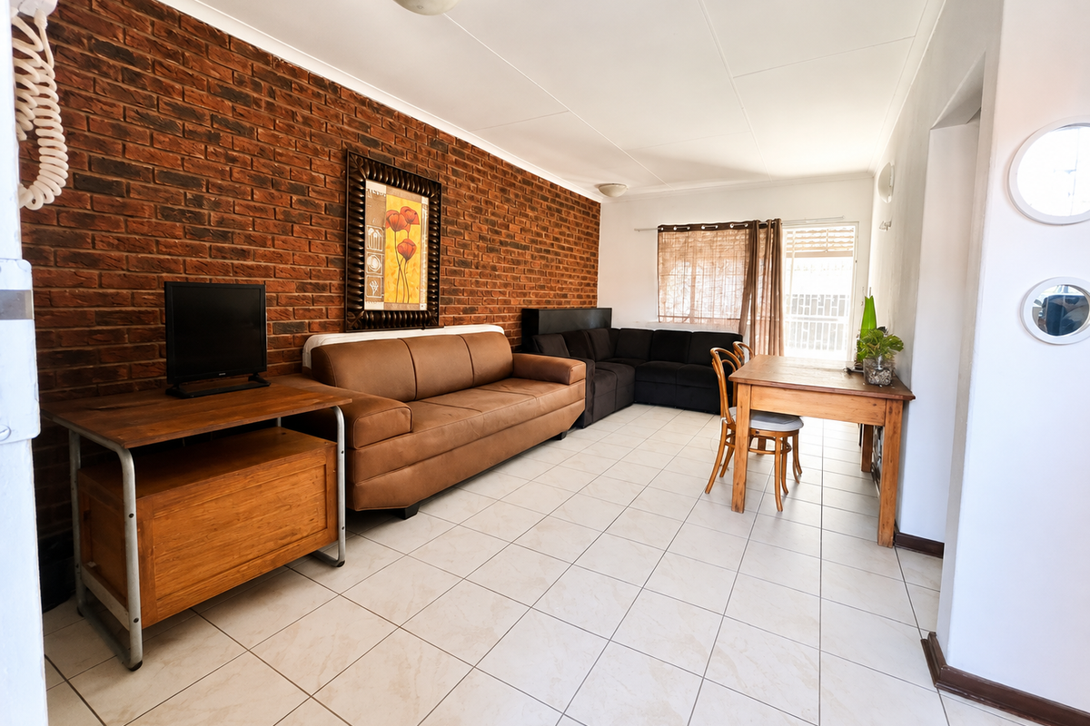 A living area featuring an exposed brick feature wall, neutral ceramic floor tiles, and direct access to an outdoor space via a sliding glass door.