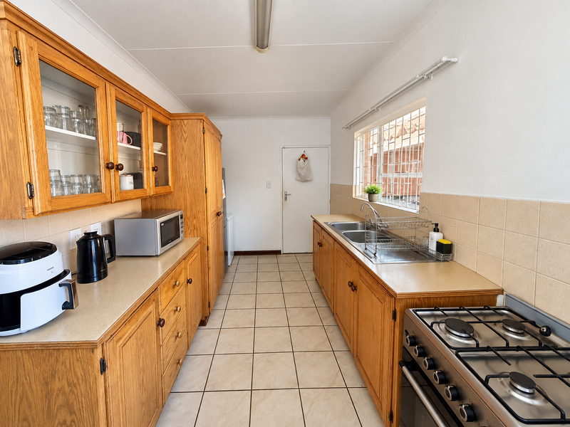 A functional galley-style kitchen featuring traditional wooden cabinetry, laminate countertops, a gas hob, and tiled flooring with ample storage space.